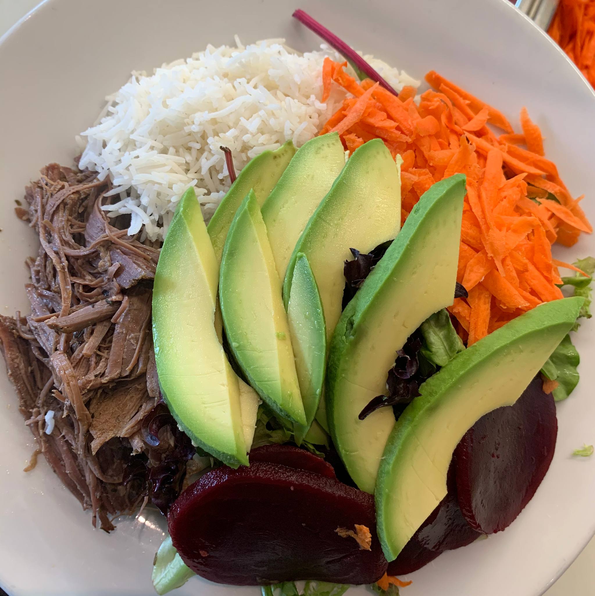 Plate of rice with shredded meat, avocado, carrot and beetroot